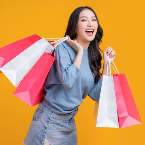 asian happy female woman girl holds colourful shopping packages standing yellow background studio shot close up portrait young beautiful attractive girl smiling looking camera with bags 609648 3029 1