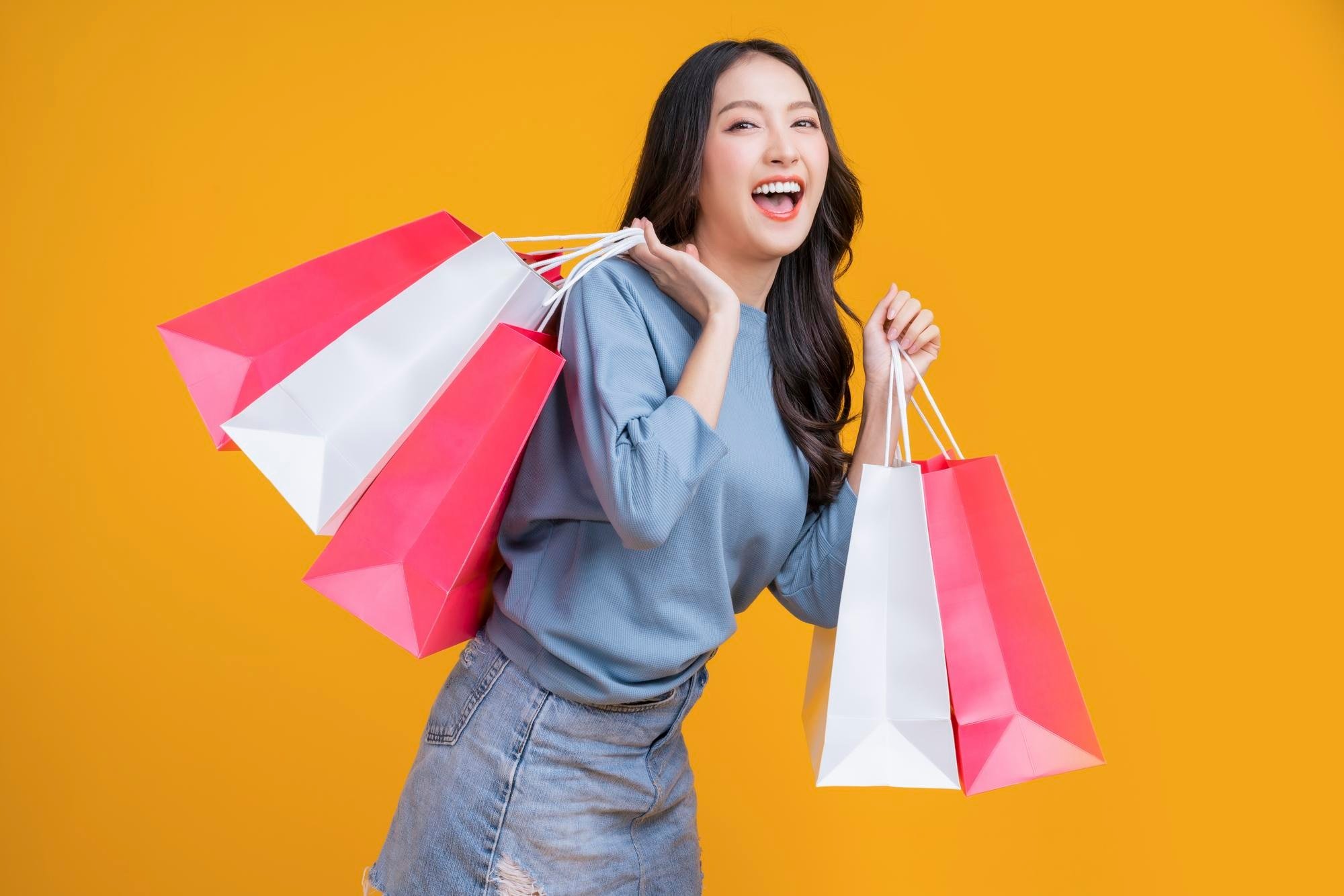 asian happy female woman girl holds colourful shopping packages standing yellow background studio shot close up portrait young beautiful attractive girl smiling looking camera with bags 609648 3029 1